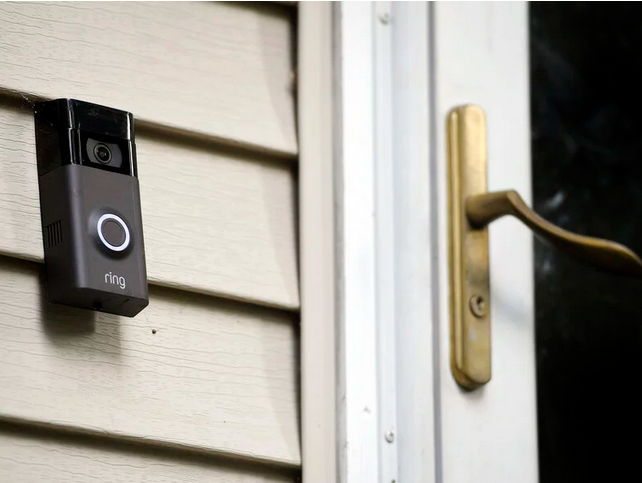 A picture of a Ring door bell unit installed on vinyl siding next to a glass security door.