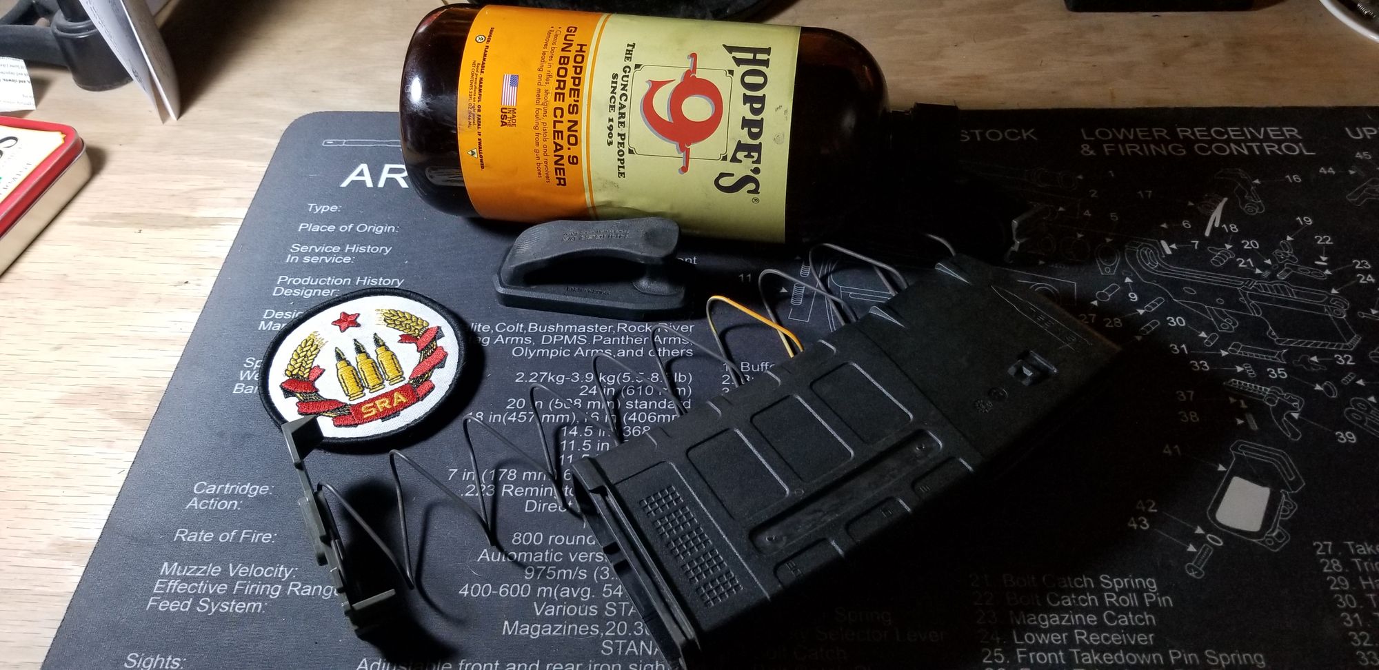 Closeup of an SRA patch, a disassembled SR-25 PMAG, and Hoppe's #9 bore cleaner laying on a gun cleaning mat.