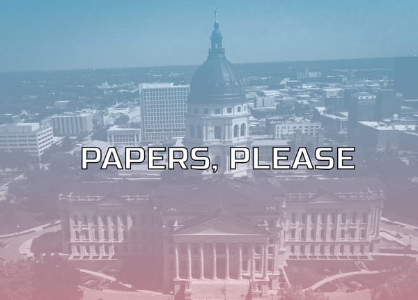 Aerial photo of Kansas state capitol with a semi transparent gradient in the colors of the trans pride flag. Caption says papers please.